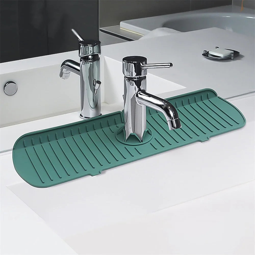A chrome silicone faucet drain mat is placed on a white countertop next to a modern kitchen or bathroom sink.