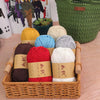 A collection of various colored crochet yarn skeins in a wooden basket, including red, blue, gray, and cream shades.