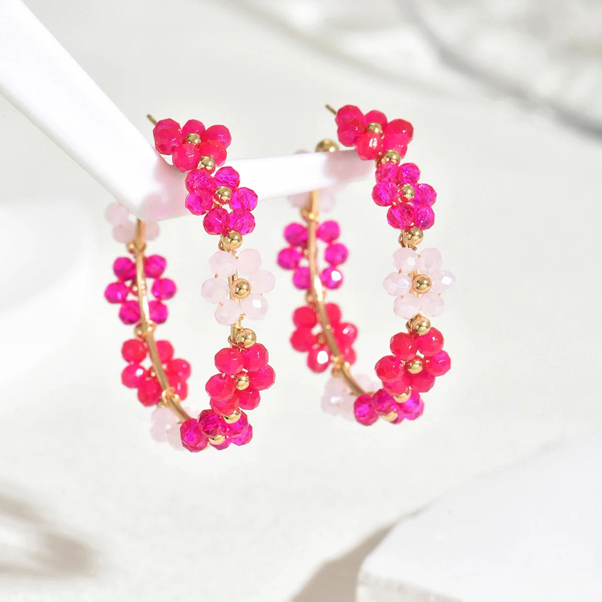 Pair of pink and magenta beaded sunflower drop earrings displayed on a white stand.