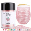 A glass jar of pink edible glitter powder next to a clear glass and a pile of various colored glitter powders.
