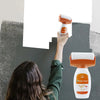 A person is using an orange and white roller paint tool to apply paint on a gray wall.