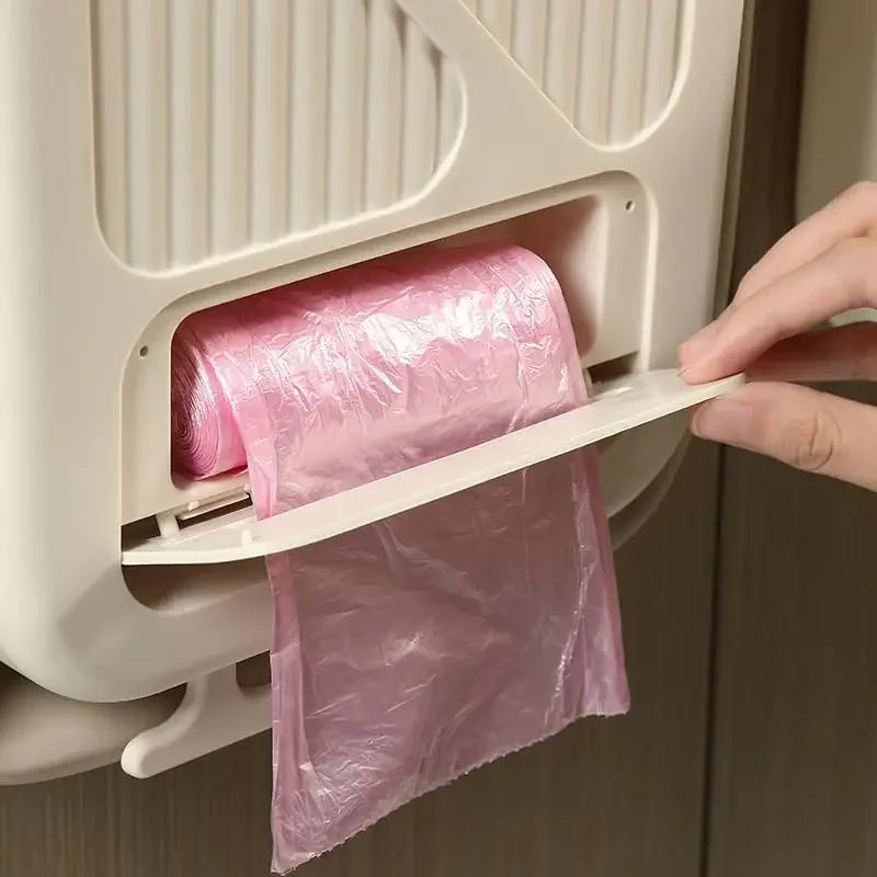 Eine Hand zieht einen rosa Plastiksack Müll aus einem weißen, hängenden, klappbaren Küchen- und Campingmülleimer.