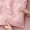 A hand is holding a pink satin quilt with a button closure, showing the fabric texture and stitching.