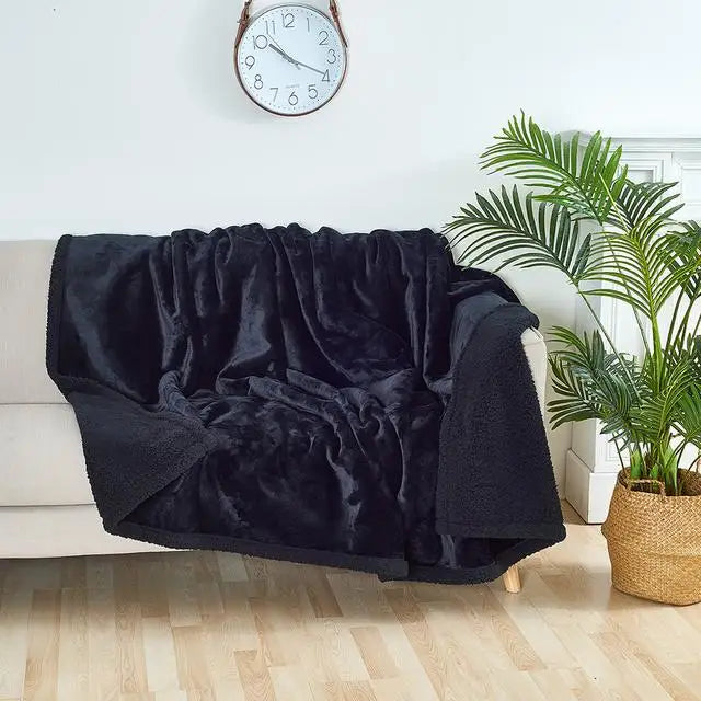 A black faux fur throw blanket draped over a white sofa next to a potted green plant.