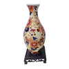 A ceramic vase with floral patterns in shades of orange, blue, and cream, displayed on a dark wooden stand.