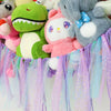 A bohemian handwoven corner toy storage net with colorful plush toys and purple, pink, and blue tassels.