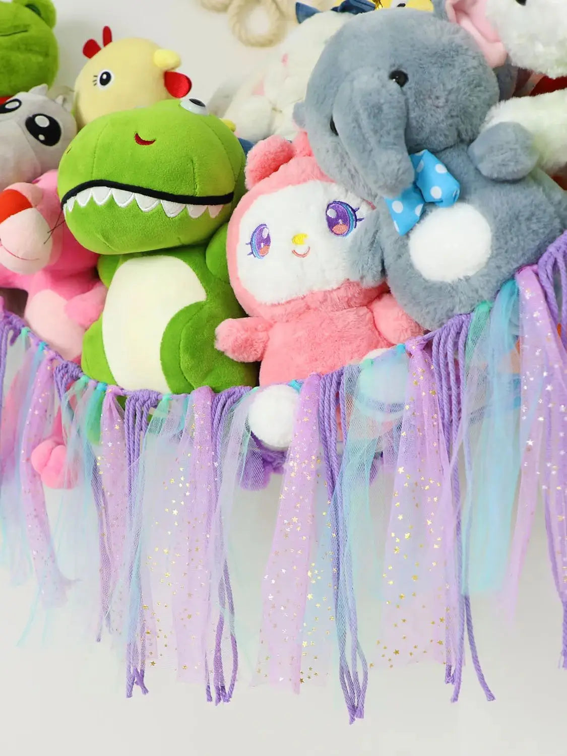 A bohemian handwoven corner toy storage net with colorful plush toys and purple, pink, and blue tassels.
