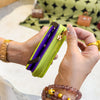 A hand holds a lime green and purple compact wallet with a gold keychain against a blurred background.