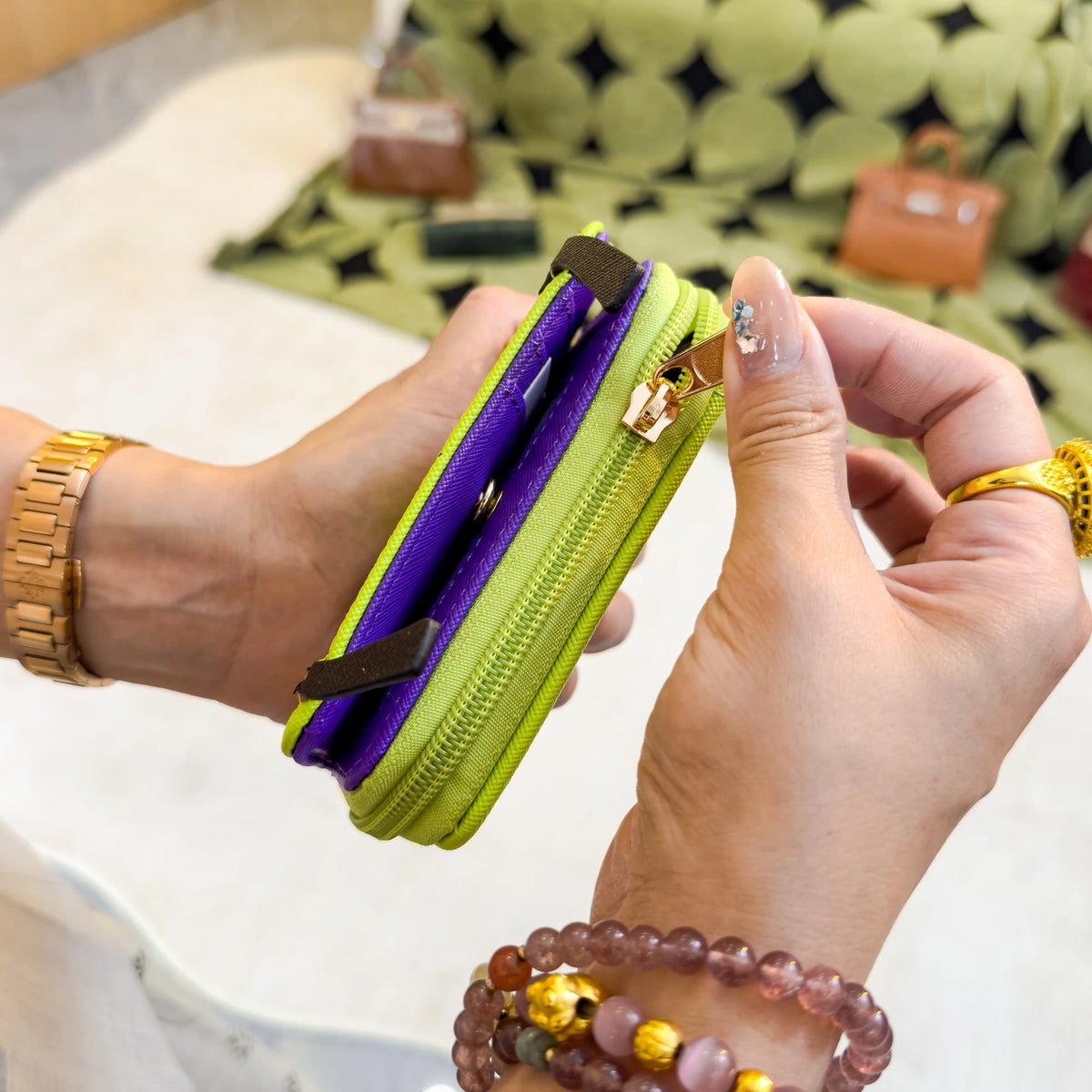 A hand holds a lime green and purple compact wallet with a gold keychain against a blurred background.