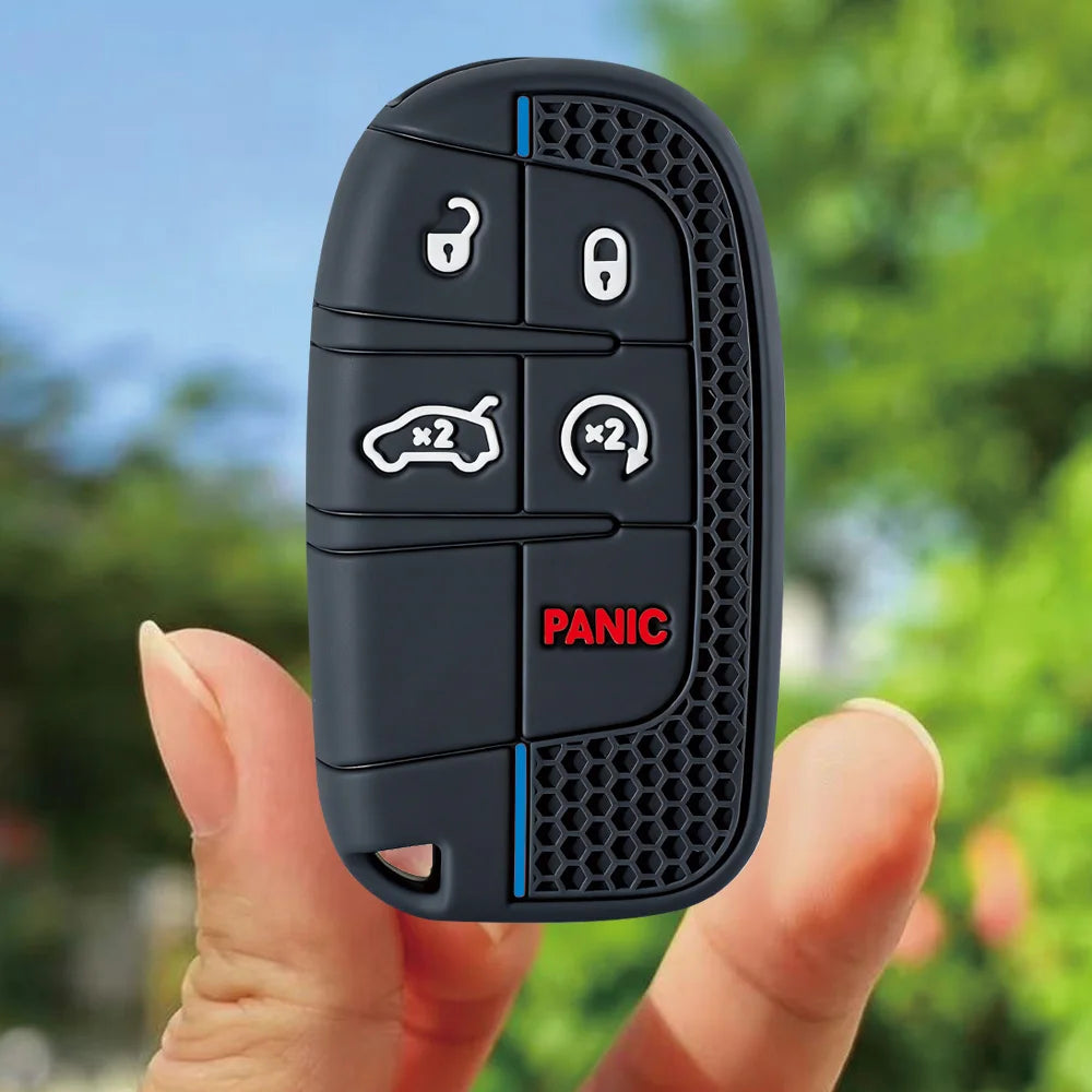 A hand holds a black silicone key fob cover with various buttons and a panic button features on the side