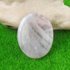 A smooth, oval, translucent white crystal stone resting on green grass next to a hand.