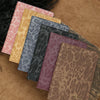 A collection of five leather passport holders in various leopard print colors and textures resting on a brown suede surface.