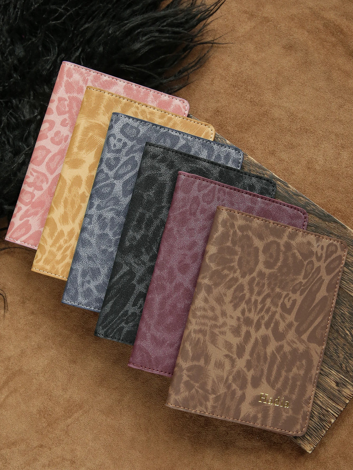 A collection of five leather passport holders in various leopard print colors and textures resting on a brown suede surface.