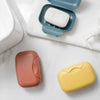 A collection of leak-proof travel soap boxes in various colors, including white, pink, and yellow, resting on a white surface
