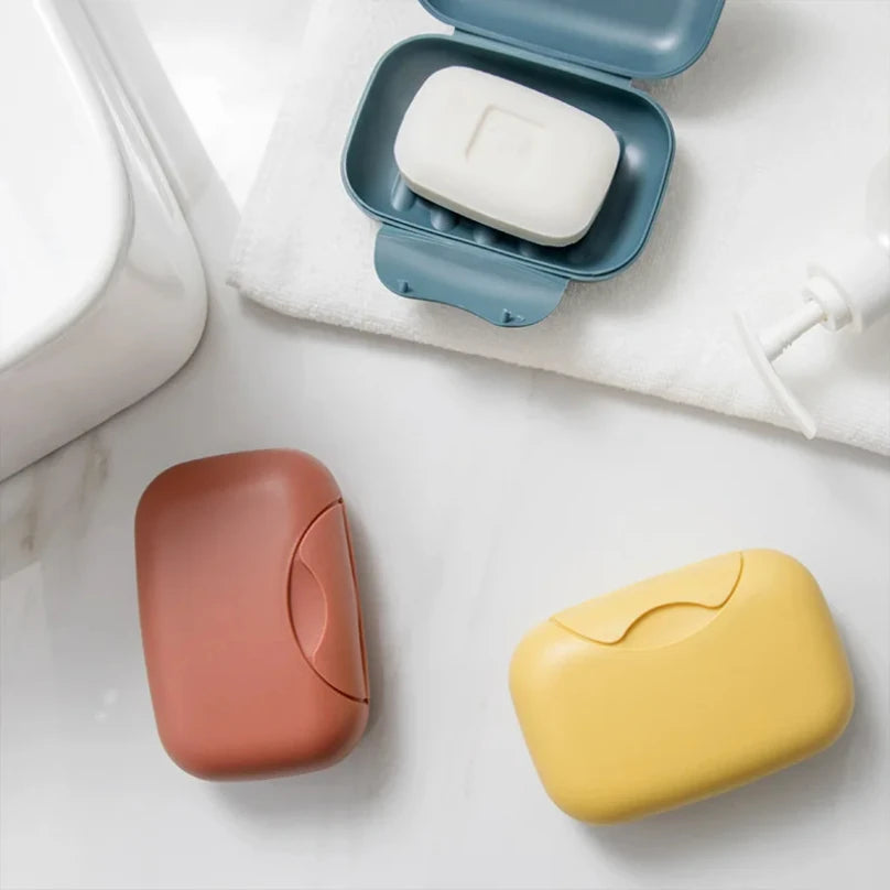 A collection of leak-proof travel soap boxes in various colors, including white, pink, and yellow, resting on a white surface