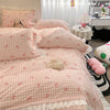 A pink and white gingham duvet cover set featuring ruffled fabric and floral embroidery on a bed.