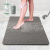 A person's legs are standing on a gray absorbent bathroom floor mat while using a lotion or soap.
