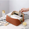 A brown leather travel makeup organizer bag is open, displaying various cosmetic bottles and makeup brushes on a white surfac