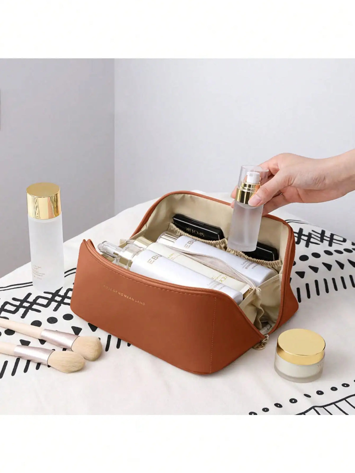 A brown leather travel makeup organizer bag is open, displaying various cosmetic bottles and makeup brushes on a white surfac