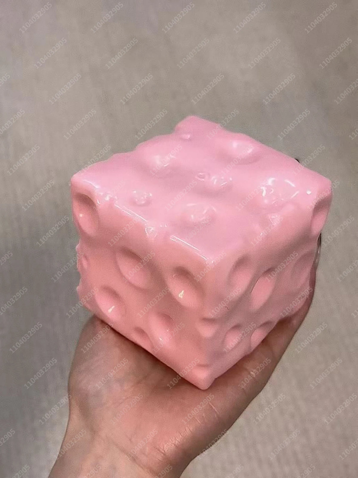 Eine rosa Jumbo-Knetball-Stressball wird in einer Hand vor einem hellgrauen Hintergrund gehalten.