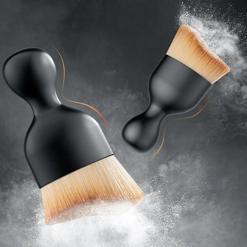 A black cleaning brush with soft bristles is shown dispersing white powder against a dark gray background.