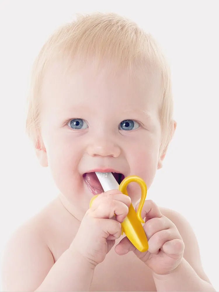 A baby is shown holding a yellow silicone banana-shaped teether and toothbrush.