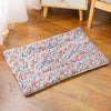 A rectangular plush pet sleeping mat with paw print patterns in soft gray and pink tones resting on a wooden floor.