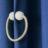 A gold-toned braided ring with pearl accents used as a magnetic curtain clip against a dark blue fabric.