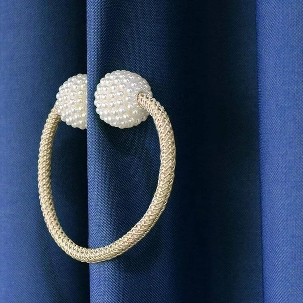 A gold-toned braided ring with pearl accents used as a magnetic curtain clip against a dark blue fabric.
