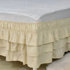 A beige adjustable elastic bed skirt with ruffled tiers is shown covering the edge of a mattress.