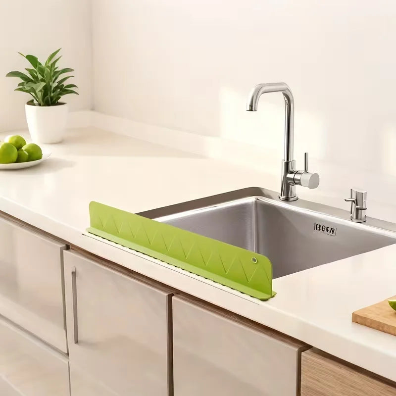 A silver kitchen sink with a modern faucet and a bright lime green silicone splash guard installed on the countertop.