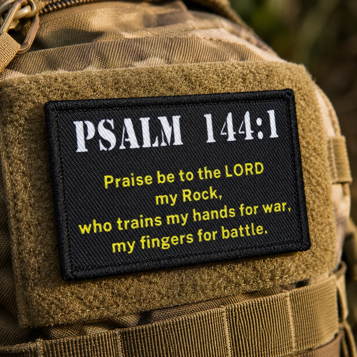 A tan military patch embroidered with Psalm 144:1 in gold thread on a canvas fabric.