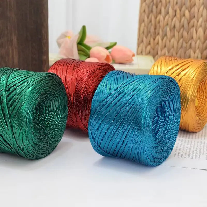 A collection of metallic flat ribbon yarn in shades of green, red, blue, and gold is displayed on a white surface.