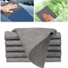 A stack of gray reusable microfiber cleaning cloths, showing a hand using one to wipe a surface.