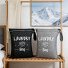 Two gray and black fabric laundry bags are displayed on a wooden rack against a white wall.