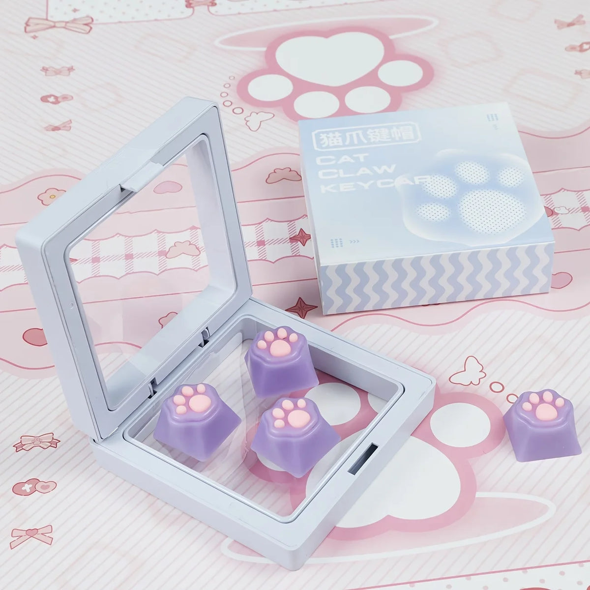 A box of silicone cat claw keycaps and several purple cat paw keycaps displayed on a pink background.