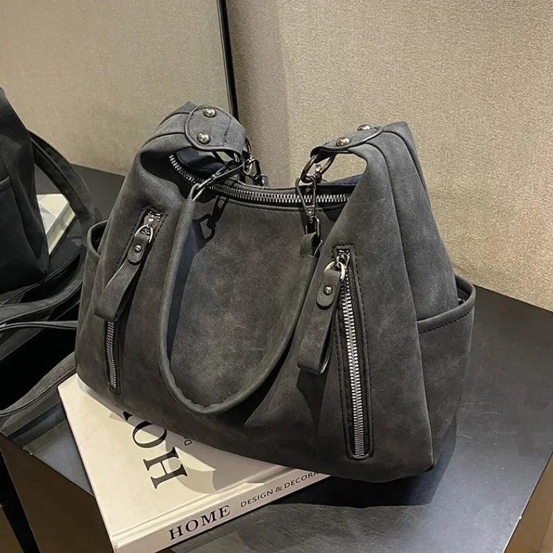 A gray matte leather crossbody hobo bag with adjustable strap displayed on a dark surface.