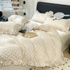 A set of three white bedding items including a duvet cover, two pillowcases, and a fitted sheet with black dot print fabric.