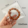 A hand holds a brown, round bead necklace inside a clear plastic jewelry pouch.