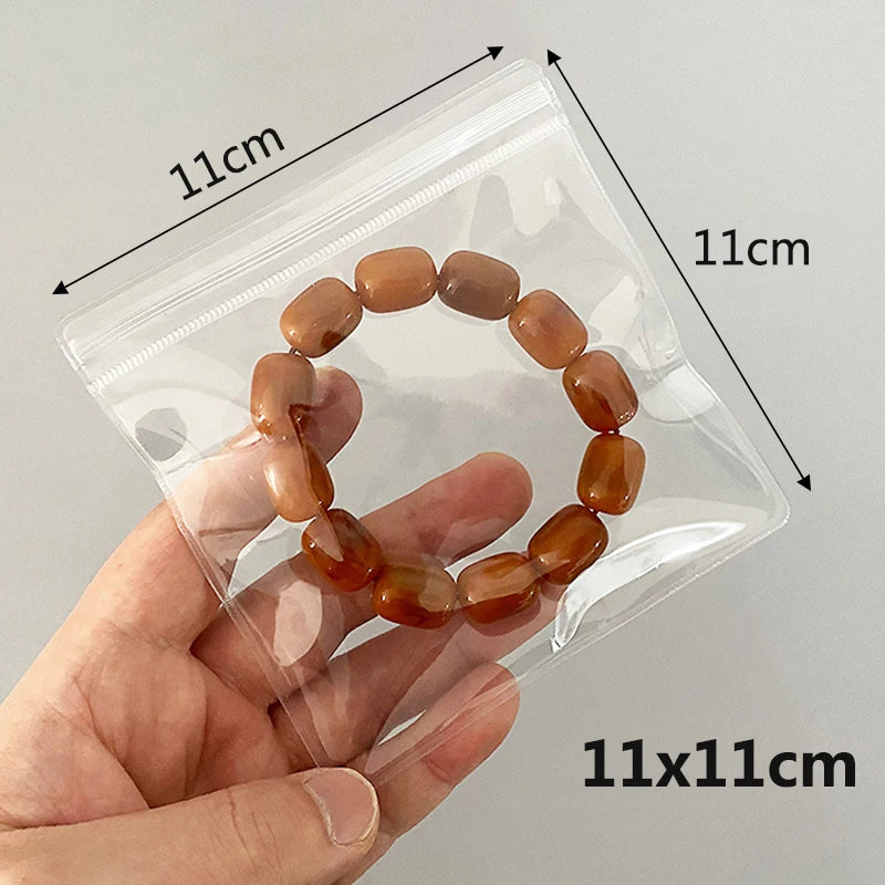 A hand holds a brown, round bead necklace inside a clear plastic jewelry pouch.