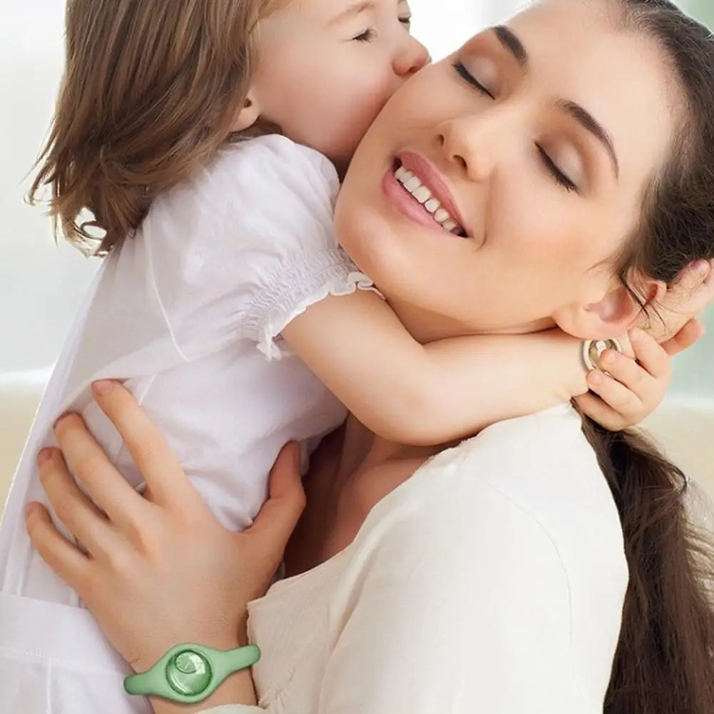 A woman gently kisses a child on the forehead while wearing a natural mosquito repellent wristband.