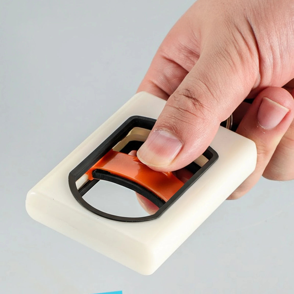 A hand is holding a white cable tie organizer with an orange strap and a black carabiner clip.