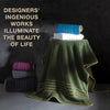 A stack of folded bath towels in teal, white, and purple rests on a green fabric drape with gold accents.