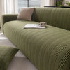 A textured olive green quilted stretch sofa cover with a light beige throw pillow and an open book on the surface.