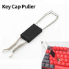 A black key cap puller tool with metal arms shown next to a mechanical keyboard.
