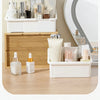 A white cosmetic organizer with multiple compartments is displayed on a wooden surface next to a vanity mirror.