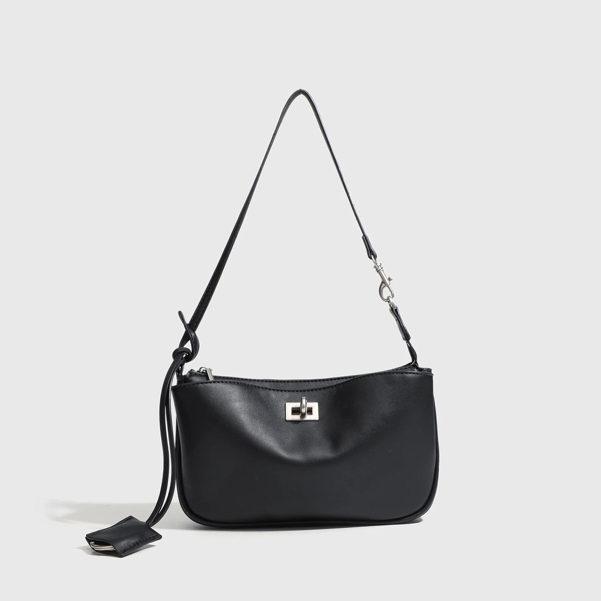 A black leather tote bag with a thin strap and a metal buckle hanging against a light gray background.