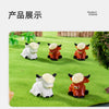 A display of four adorable resin Highland cow figurines in white and orange colors set against a green grassy background.