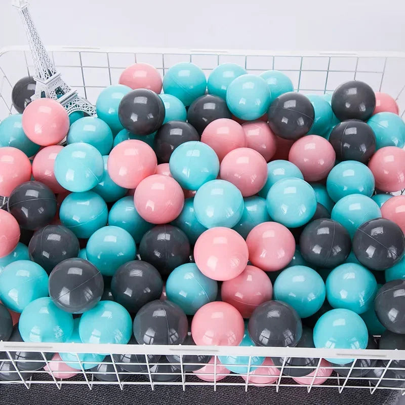 A large quantity of colorful plastic ball pit balls in shades of pink, blue, and gray are displayed in a white wire basket.