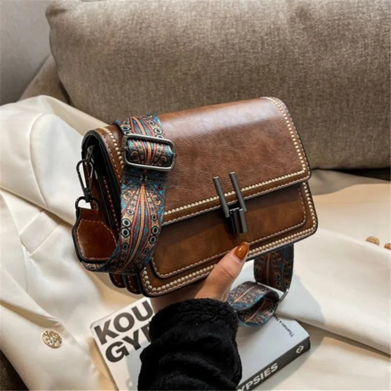 A brown leather mini cross-body bag with a patterned strap resting on a white fabric surface.